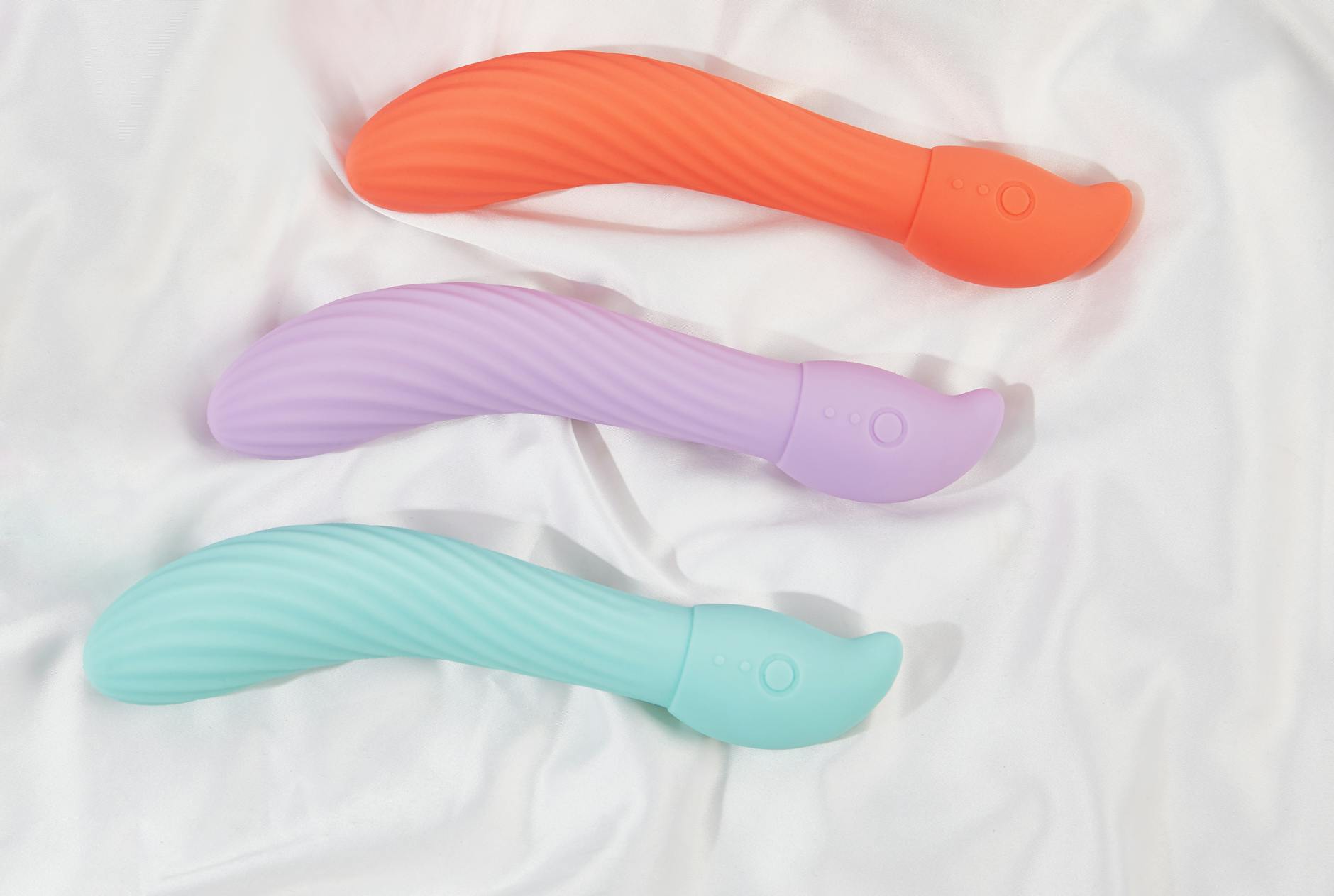 A teal silicone clitoral vibrator resting on white silk fabric