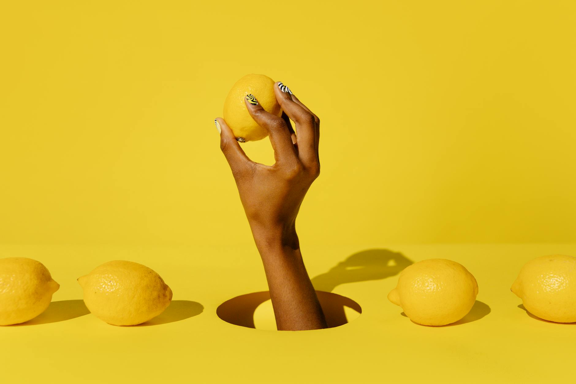 A hand holding a fresh lemon against a bright yellow background, symbolizing renewal and vitality