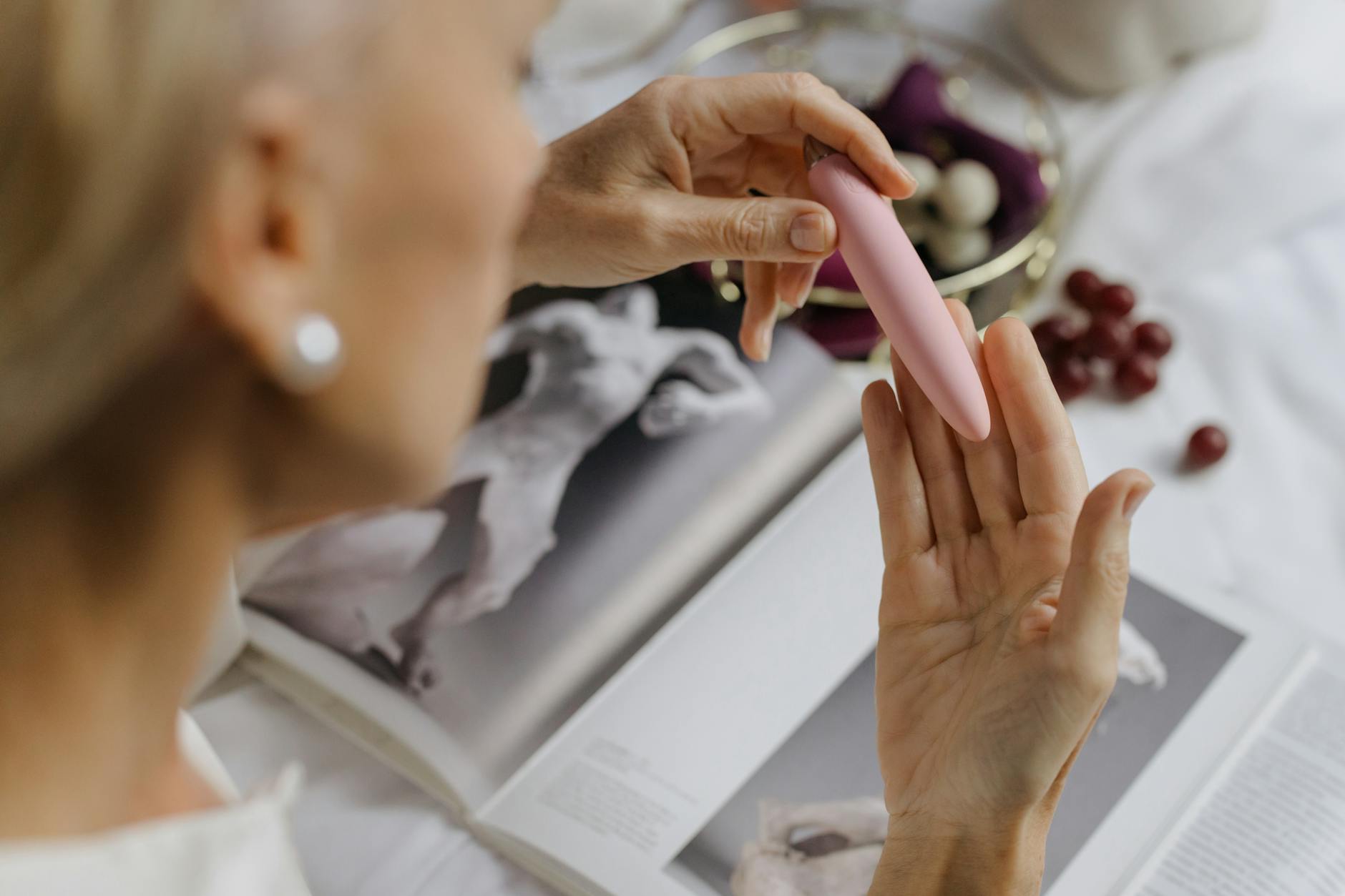 Close-up of a woman with a pink vibrator surrounded by books, symbolizing the personal journey of sexual self-discovery and confidence rebuilding.
