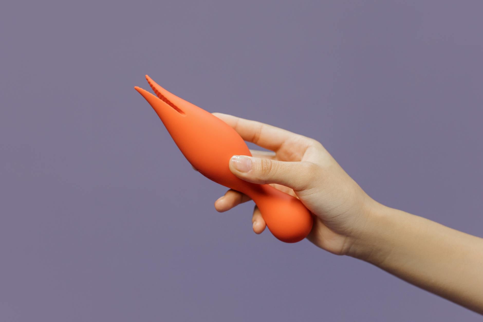 Close-up of a hand holding a lemon-colored vibrator against a purple backdrop, showcasing the design of a clitoral toy