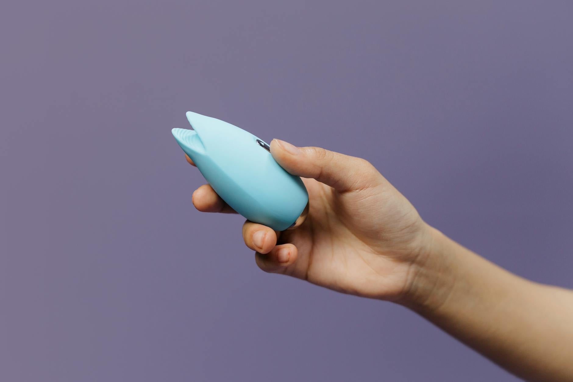 A blue silicone vibrator held in hand against a purple background, promoting self-love and sexuality.