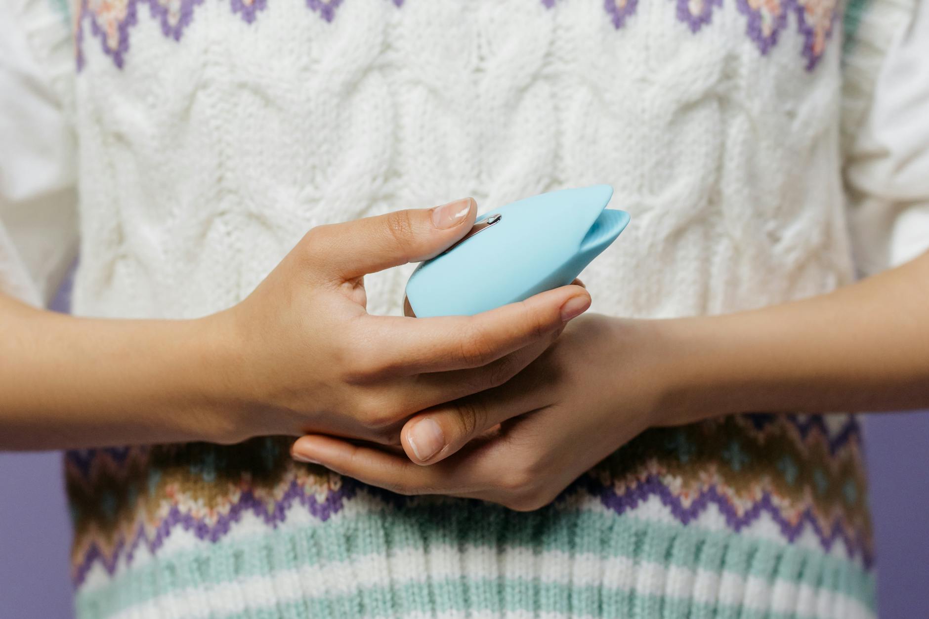 Close-up of hands holding a sleek blue vibrator against a purple background, illustrating gentle toy handling