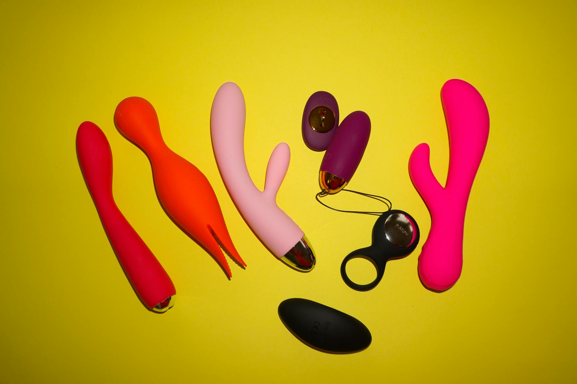 Hands holding pink and blue silicone vibrators together against a pastel background